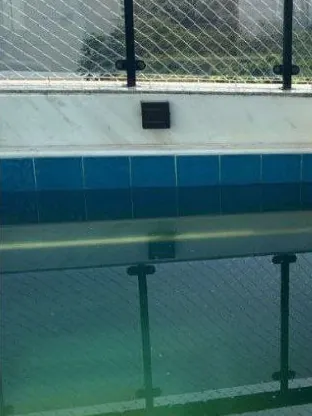 Antes: piscina com vidro e rede de proteção em volta, a água escura