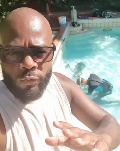 O profissional da Oliveira Piscinas falando na beira da piscina cheia, com outro profissional de máscara e cilindro trabalhando no fundo
