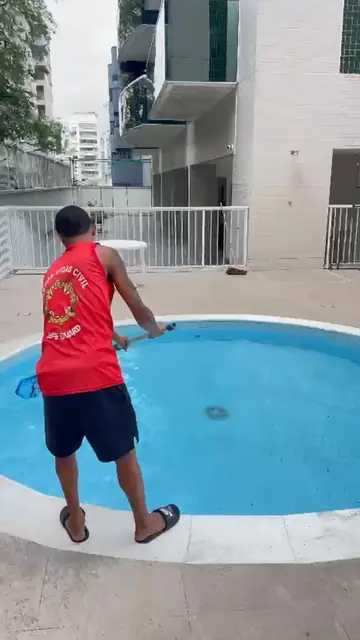 O guarda-vidas de costas, de regata vermelha, na beira da piscina redonda de um condomínio