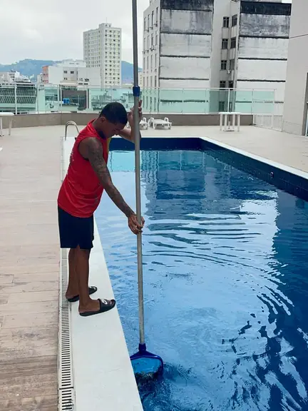 Guarda-vidas de regata vermelha passando a peneira na piscina da cobertura de um prédio