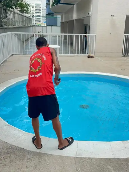 Guarda-vidas de regata vermelha, de costas, passando a peneira na piscina redonda de um condomínio