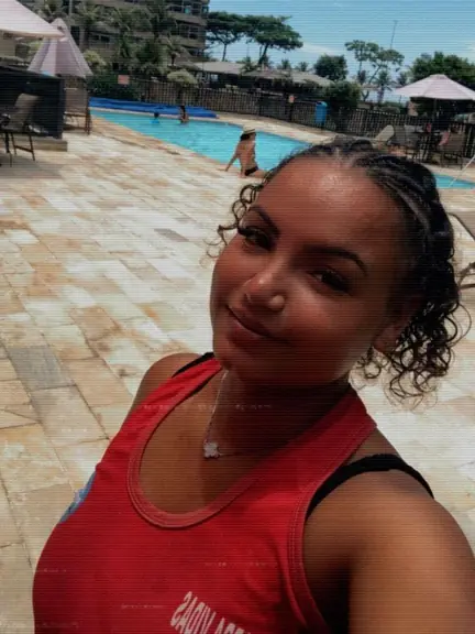 Guarda-vidas de regata vermelha numa piscina de clube, com prédios e palmeiras atrás