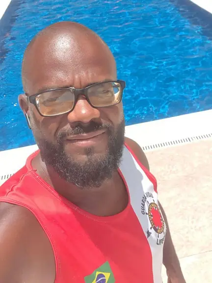 Guarda-vidas de óculos e regata vermelha na beira de uma piscina de condomínio